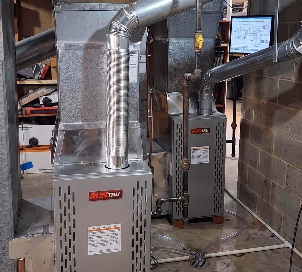 Two RUNTRU furnaces connected to ventilation pipes installed in a basement with concrete walls and floor.