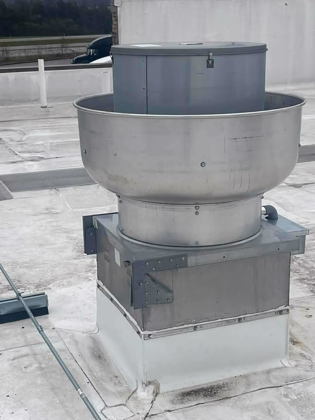 Large industrial rooftop ventilation fan made of metal on a flat roof with a white covering.