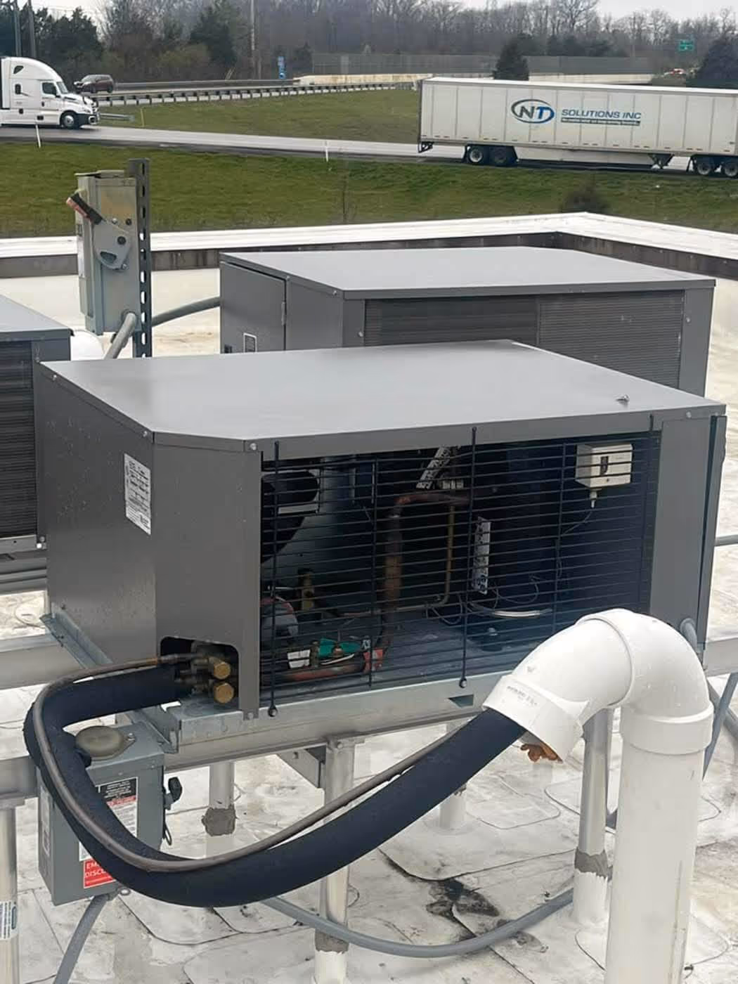 Two rooftop HVAC units with visible coils and connected insulated piping on a white flat roof.