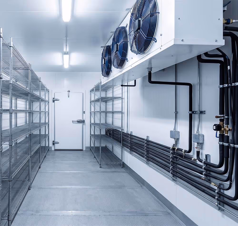 Empty industrial walk-in fridge with metal shelves and cooling fans on the ceiling.